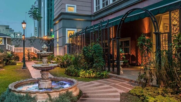 A courtyard with a stone fountain, a pathway, and a building with a covered entrance. - Travelers Safari - Westlands (Nairobi)