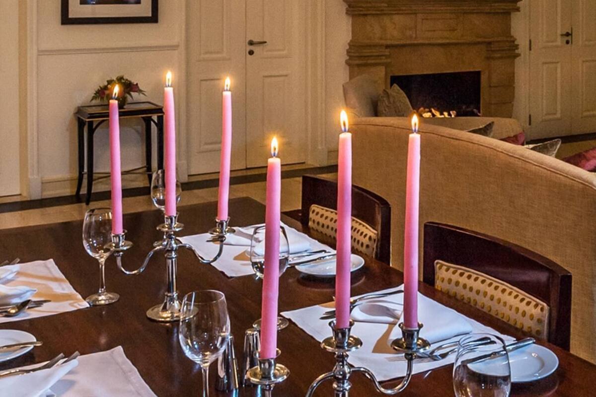A dining table set for six with pink candles, a fireplace, and patterned carpet.