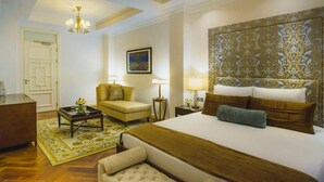 A hotel room with a large bed, a sitting area with a chair and a small table, a desk, and a patterned headboard. - Travelers Safari - Westlands (Nairobi)