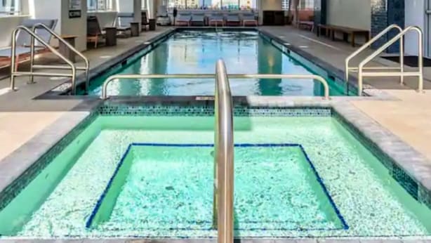 A large indoor swimming pool with clear blue water, surrounded by lounge chairs and a city view. - Premier Studio with King Bed and Queen Sofa-bed (Miami)