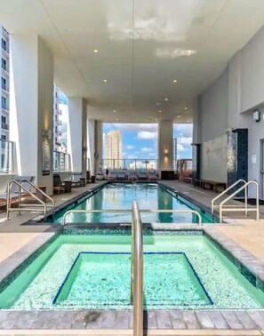 Une grande piscine intérieure à l’eau d’un bleu limpide, entourée de chaises longues et offrant une vue sur la ville.