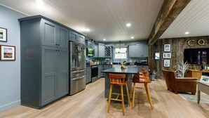 A modern kitchen with grey cabinets, stainless steel appliances, and a central island with bar stools. - Camp Quality Time on Wilson Lake 3-bedroom, hot tub (Wilton)