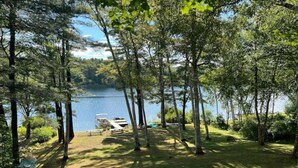 A lakeside cabin with a dock, surrounded by trees and a grassy area. - Camp Quality Time on Wilson Lake 3-bedroom, hot tub (Wilton)