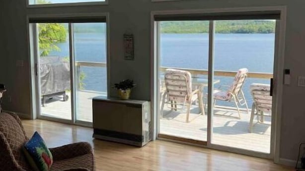 A spacious living room with a large sliding glass door leading to a balcony with a view of a lake. - Camp Serenity
 (Wilton)