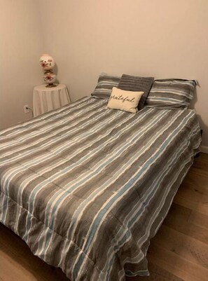 A bed with striped bedding and a pillow with the word "grateful" on it.