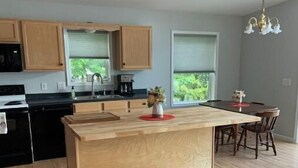 A modern kitchen with wooden cabinets, a central island, and a dining area with a table and chairs. - Camp Serenity
 (Wilton)
