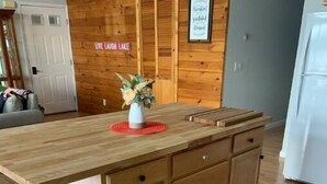 A wooden kitchen island with a countertop and drawers, a vase with flowers, and a sign above reading "CAMP". - Camp Serenity
 (Wilton)