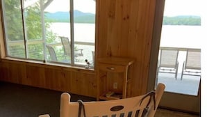 A wooden interior with a rocking chair, large windows, and a view of a lake. - Camp Serenity
 (Wilton)