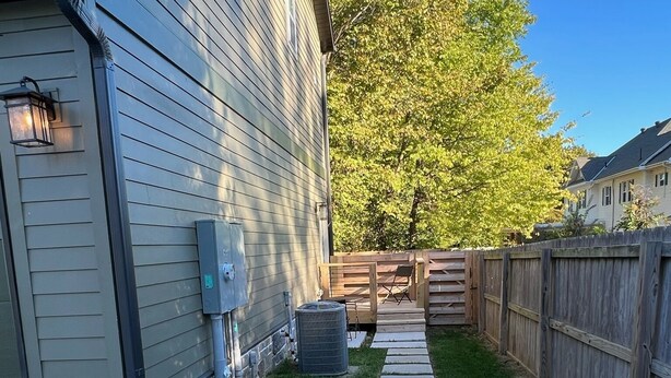 A backyard with a stone pathway leading to a wooden deck, surrounded by a wooden fence and a house with siding.