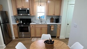 A modern kitchen with wooden cabinets, stainless steel appliances, a round dining table with white chairs, and a window providing natural light.