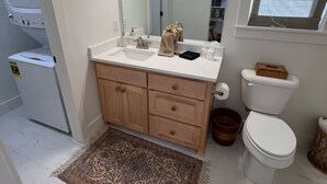 A bathroom with a white sink, wooden cabinets, a large mirror, a toilet, and a small window.