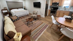 A compact living space with a bed, sofa, dining table, and kitchenette.