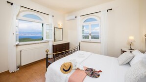 Ein Schlafzimmer mit einem großen Bett, zwei Fenstern mit Vorhängen, einem Schminktisch und einer Heizung, mit Blick auf die Landschaft.