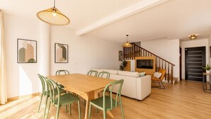 Un intérieur moderne avec une table à manger en bois, des chaises vertes, un canapé, un téléviseur et un escalier.