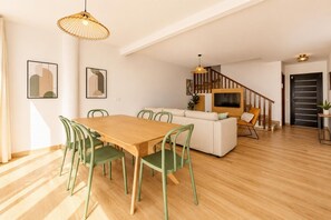 Un interior moderno con una mesa de comedor de madera, sillas verdes, un sofá, un televisor y una escalera.