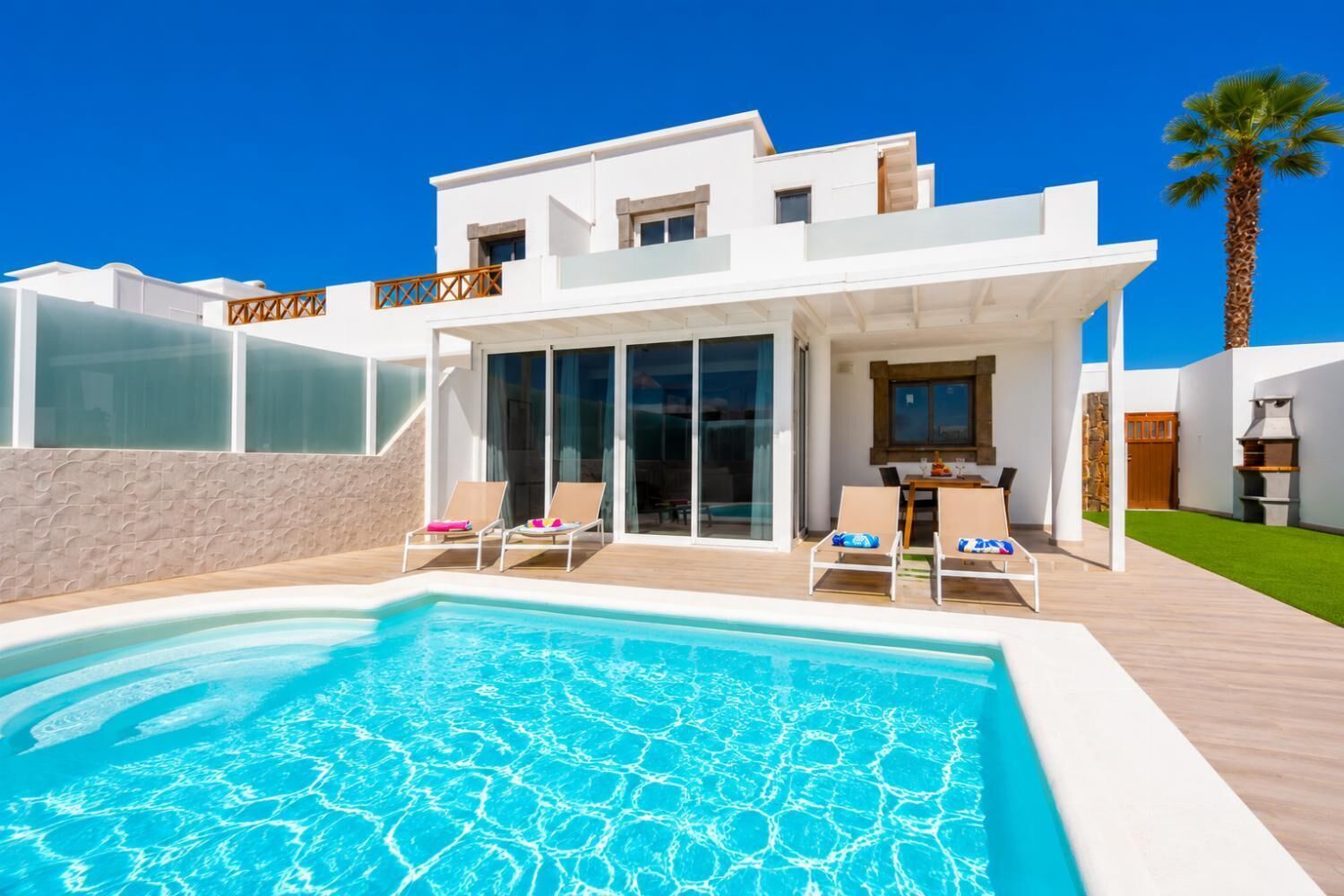 A modern house with a swimming pool, lounge chairs, and a barbecue area.