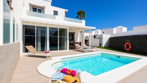 Un espace moderne aménagé au bord de la piscine, avec une piscine à l’eau d’un bleu limpide, des chaises longues et un chapeau de soleil posé sur une serviette.