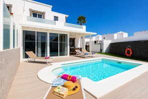 Un área moderna junto a la piscina con una piscina azul cristalina, sillas de descanso y un sombrero de sol sobre una toalla.