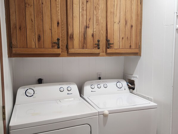 A laundry area with two white front-loading washers and dryers, wooden cabinets above, and a white tiled backsplash. - Quiet Retreat. 5 Minutes to the Marina and Boat Ramp and Pet Friendly! (Eufaula)