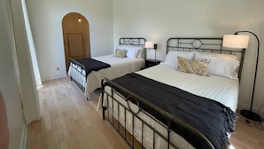 A bedroom with two beds, a wooden floor, and a door leading to another room.