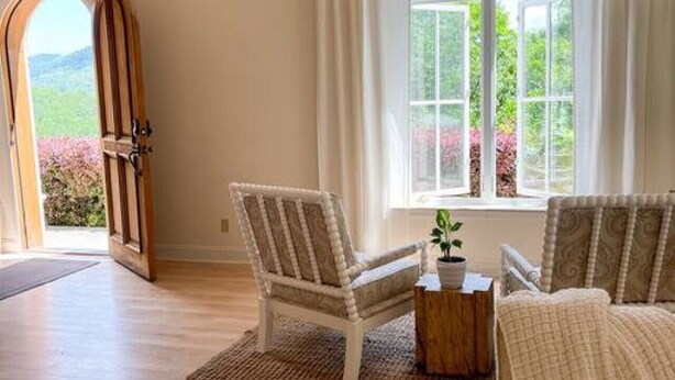 A spacious room with a large window, a wooden door, and a cozy seating area with a sofa and two chairs.
