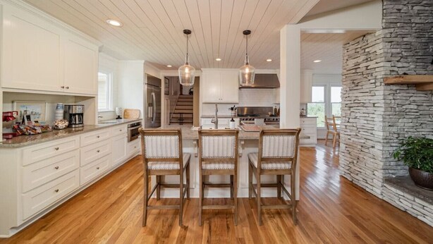 A spacious kitchen with wooden flooring, white cabinetry, and a central island with chairs.