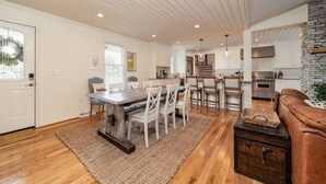 A spacious living area with a dining table, chairs, a brown leather sofa, and a stone accent wall.
