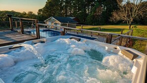 A hot tub with a wooden deck and a view of a house and trees in the background.