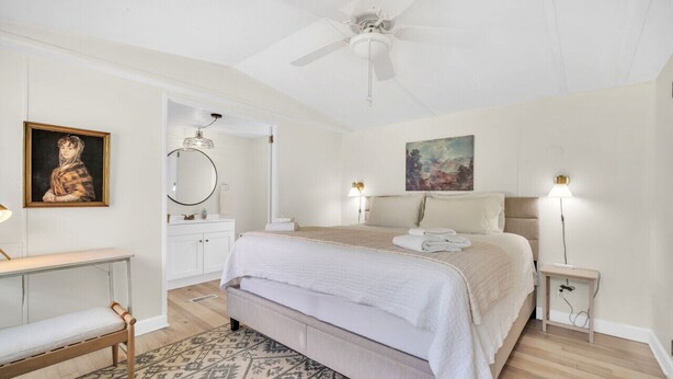 A bedroom with a bed, bedside tables, a desk, a ceiling fan, and artwork on the walls.