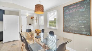 A modern kitchen with a glass dining table, white appliances, and a chalkboard sign detailing local attractions.
