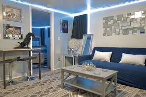 A modern living room with a blue sofa, a coffee table, and a bar area with stools.