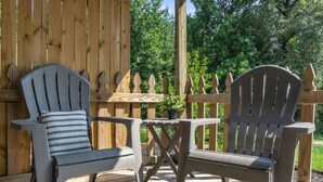 Two Adirondack chairs with striped cushions on a wooden deck, a small table, and a wooden fence in the background. - Cozy, Bright Suite w/ King Bed (Travelers Rest)
