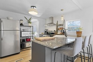 A modern kitchen with a stainless steel refrigerator, a microwave, a stove, and a large granite island with bar stools. - The Traveler’s Rest Stop (Travelers Rest)