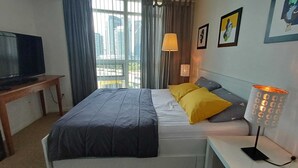 Een hotelkamer met een bed, een televisie op een standaard, een lamp en een raam met gordijnen.