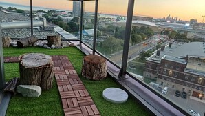 Een dakbalkon met een pad van baksteen, houten blokken en uitzicht op de stad.