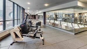 Een fitnessruimte met cardioapparaten, grote ramen en een glazen wand met uitzicht op een stadsbeeld.