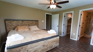 Une chambre avec une tête de lit en bois, un lit avec une literie beige, un ventilateur de plafond et un sol carrelé.