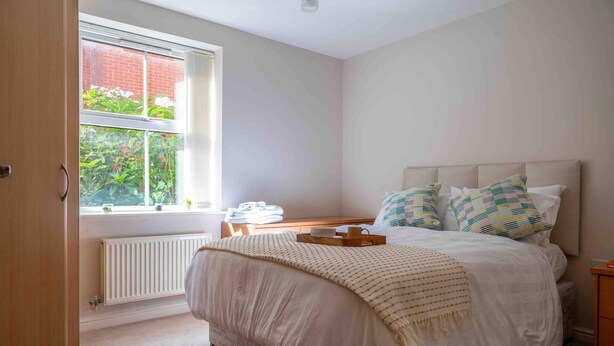 A bedroom with a bed, a window, a radiator, and a bedside table. - Closetocitycentre&nec-business&family-freeparking (Solihull)