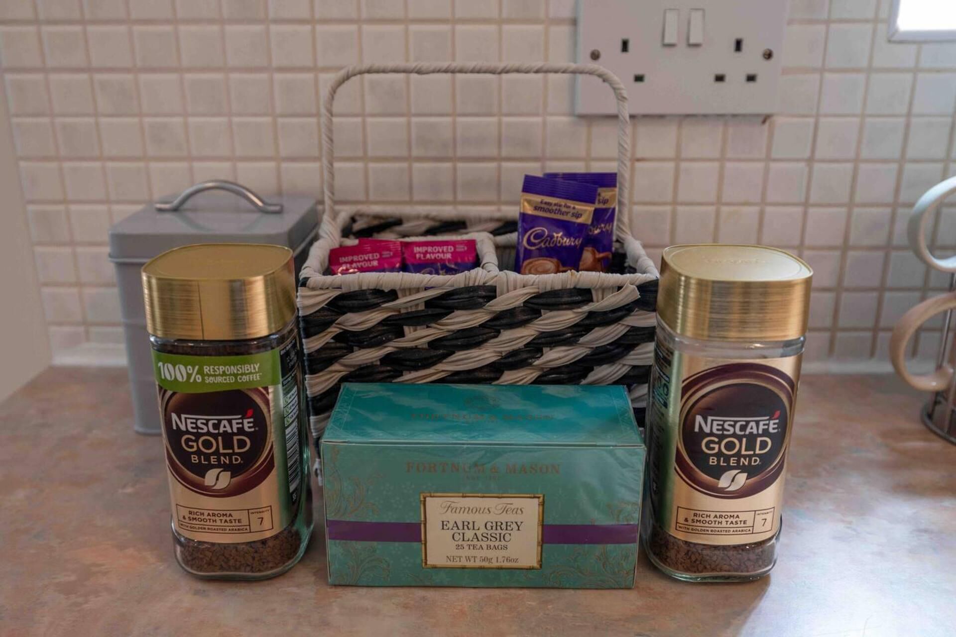 Een keukentafel met een mandje met theezakjes, een doos Earl Grey thee en twee Nescafé Gold Blend koffieblikken.