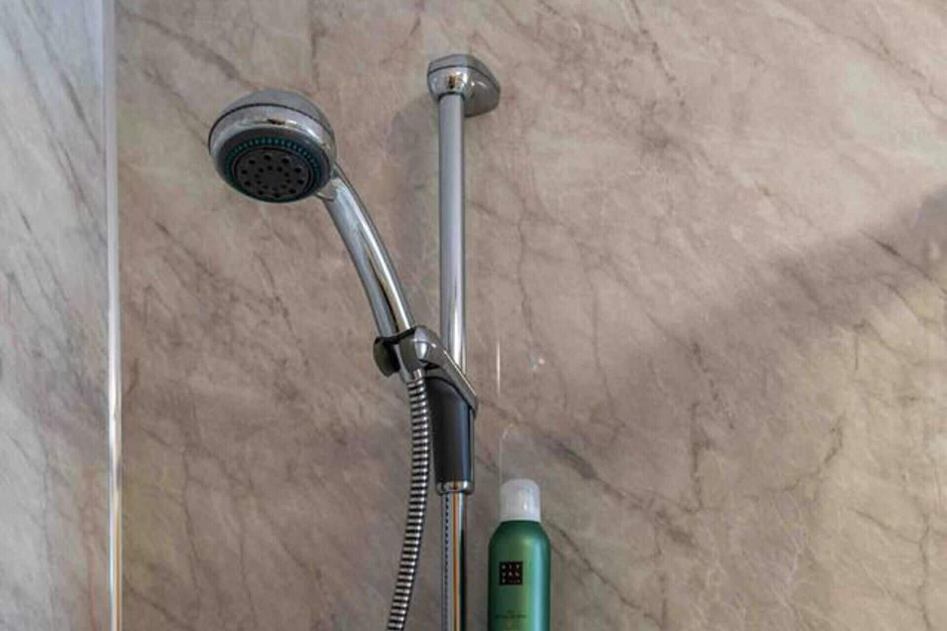 A shower with a handheld showerhead and a fixed overhead showerhead, both mounted on a wall with a marble-like texture.