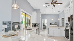 Una cucina moderna con mobili bianchi, una grande isola centrale e una ventola a soffitto.