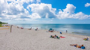 Una spiaggia con una rete da pallavolo, persone che prendono il sole e cielo sereno.