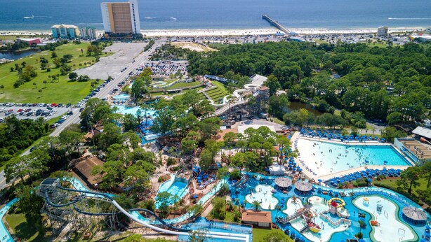 An aerial view of a resort with multiple swimming pools, water slides, and a beach area.