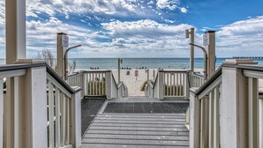 A wooden staircase leading to a beach with a clear view of the ocean and a cloudy sky.