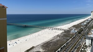 A beach with a pier extending into the ocean, a sandy beach, and a road running parallel to the beach.