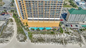 A multi-story hotel with a pool area, located near a beach.