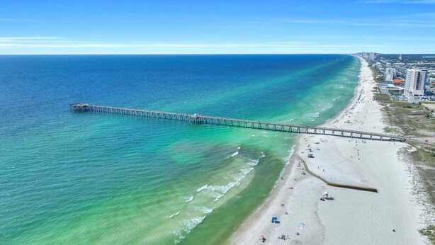 A coastal beach with a long pier extending into the ocean.