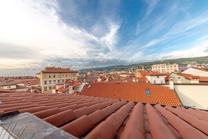 Panoramica urbana con tetti rossi in tegole e diversi edifici, tra cui un edificio giallo di rilievo con numerose finestre.