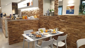 A breakfast area with a brick wall, a counter with food items, and a table set for two with breakfast plates. - Hotel Mura 5&7 (Trieste)