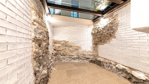 A narrow, enclosed space with white brick walls and a stone floor, featuring a skylight and a glass railing above. - Hotel Mura 5&7 (Trieste)